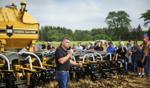 A presenter speaks into a microphone at the Outdoor Canada Farm Show, demonstrating agricultural equipment to a crowd of attendees.