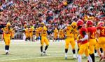 University of Guelph football players in yellow and blue uniforms face off against red team members on the field, with a cheering crowd in the background during a homecoming game.