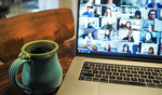 Green ceramic mug beside a laptop displaying a video conference with multiple participants.