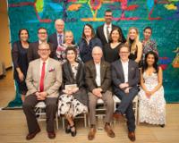 A group photo of the Board of Directors for the University of Guelph Alumni Association, standing and sitting in front of a colorful backdrop. The group includes 12 people, dressed in formal attire, smiling for the camera.