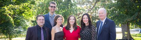 Group photo of University of Guelph staff at an outdoor event, featuring six individuals dressed in formal attire, standing in front of a lush green background.