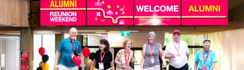 Group of University of Guelph alumni smiling and standing under a 'Welcome Alumni' banner during Alumni Reunion Weekend.