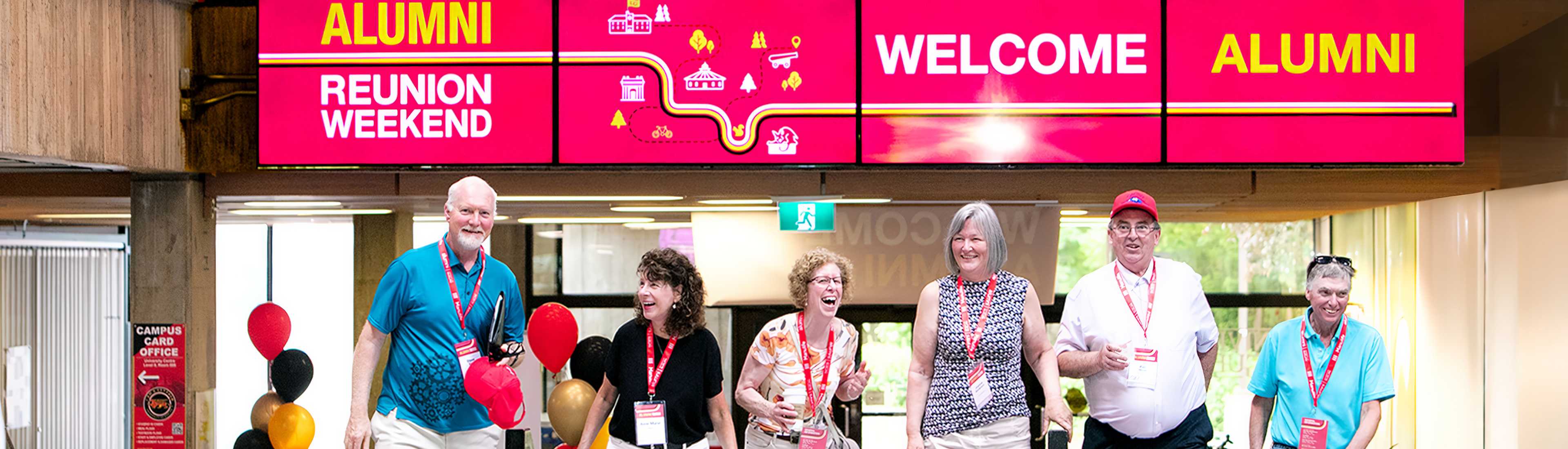 Group of University of Guelph alumni smiling and standing under a 'Welcome Alumni' banner during Alumni Reunion Weekend.