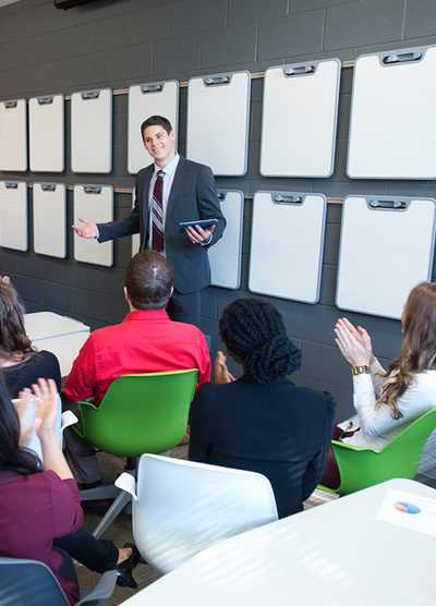 Young alumni listening to a speaker at the front of the class.