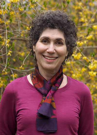 Portrait of Alumni of Honour Award winner Barbara Salsberg Mathew, smiling and standing in front of a background of yellow flowers.