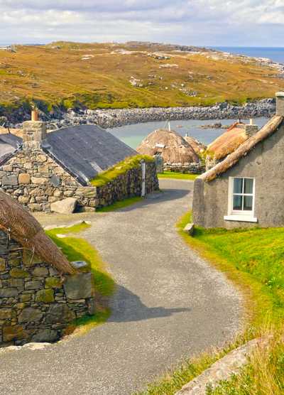 Traditional stone houses with thatched roofs in a picturesque coastal village on a Scottish isle, surrounded by rugged landscapes and ocean views.