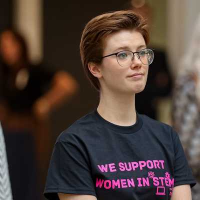 Group of individuals attending a STEM event, with one person wearing a black t-shirt that reads 'We Support Women in STEM' in bold pink text.